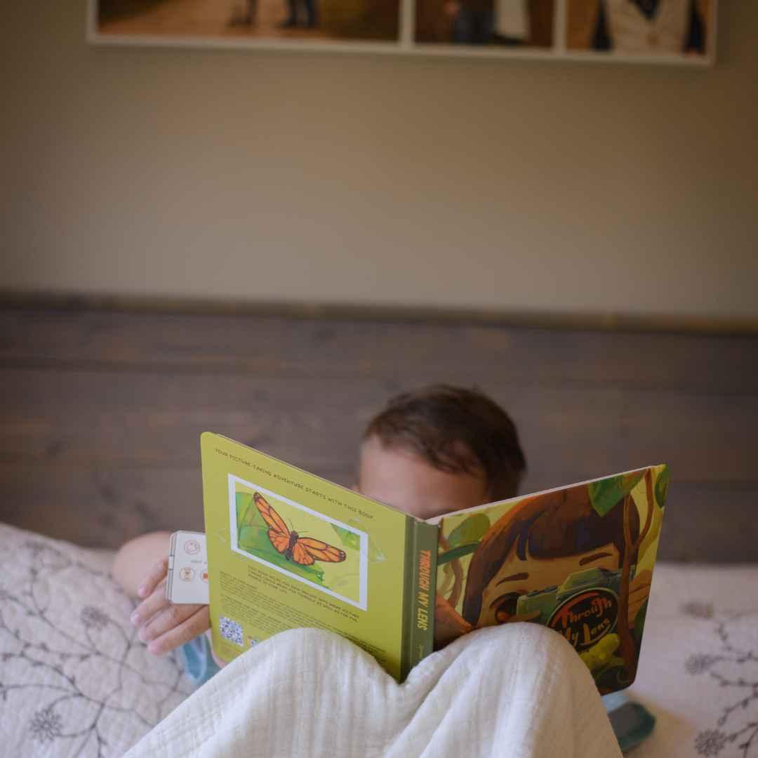 A child reads an open activity book titled "Through My Lens" with a butterfly illustration.