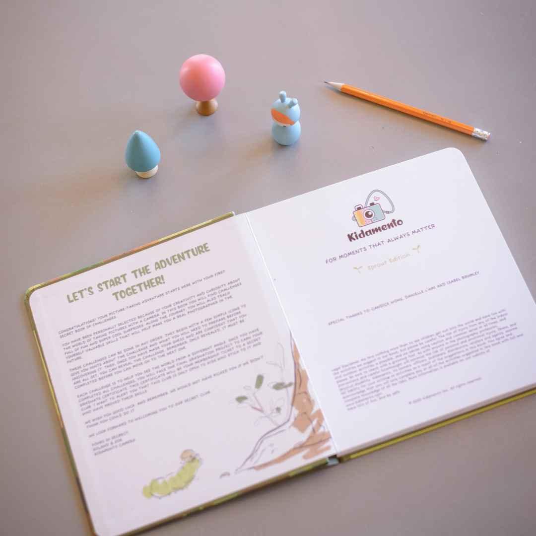 An open activity book with a camera logo, a pencil, and two small wooden toys.