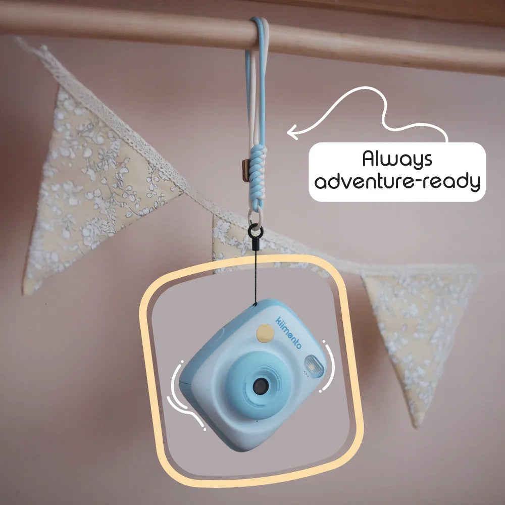Sky blue instant print camera with a wrist strap hanging from a wooden rod.