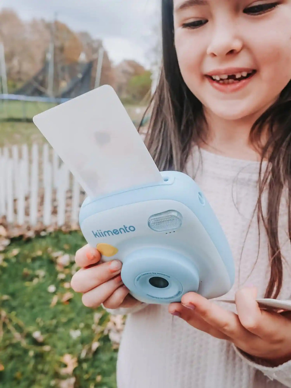 Girl holding kiimento Sky Blue Print Pro Camera Model P2 printing a photo outdoors